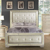 Cama King Loraine con cabecera y piecera tapizadas capitoneadas en tono champagne, marco con detalles espejados y remaches decorativos, ambientada en recámara con cómoda y buró a juego, lámpara de mesa y ropa de cama con estampado de hojas grises - Estylo House Muebleria