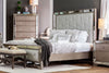 Cama King Loraine con cabecera tapizada capitoneada en tono gris y marco con acabado espejado, ambientada en recámara con cómoda y burós a juego, banca tapizada a los pies de la cama, ropa de cama en tonos grises y blancos, lámparas de mesa y tapete - Estylo House Muebleria