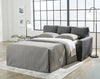 Sofá Cama Matrimonial Rannis extendido como cama con cubrecama gris acolchado, tapizado gris oscuro, en ambiente con ventanal, lámpara de piso y cuadros decorativos - Estylo House Muebleria