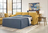 Sofá Cama Queen Keerwick extendido como cama con ropa de cama azul marino, tapizado mostaza, en sala con mesa lateral de madera, lámparas y cuadro abstracto - Estylo House Muebleria