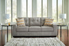 Sofá Cama Queen Storrow en su forma de sofá, tapizado gris con cojines decorativos en estampado geométrico naranja, en sala con mesas laterales, lámparas y tapete texturizado - Estylo House Muebleria